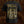 A black short-sleeve Brodequin t-shirt shown from the back, featuring a large distressed gold graphic print with the text 'Perpetualion of Suffering' and 'unmatched brutality' over a dark medieval-style illustration. The shirt is displayed against a dark, textured brown background.